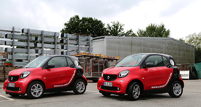 Foto: Zwei rote Elektrofahrzeuge (smart) stehen nebeneinander auf dem Firmenparkplatz